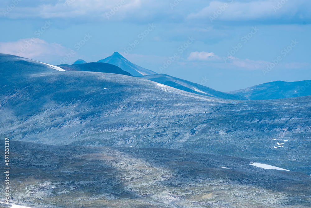 Wild barren mountain tops in a vast empty polar landscape of northern Norway. In the distance a pointy peak, as a view from Bolnatind, Helgeland, Norway. Fjell of the arctic circle. Cold blue mountain Wild barren mountain tops in a vast empty polar landscape of northern Norway. In the distance a pointy peak, as a view from Bolnatind, Helgeland, Norway. Fjell of the arctic circle. Cold blue mountain