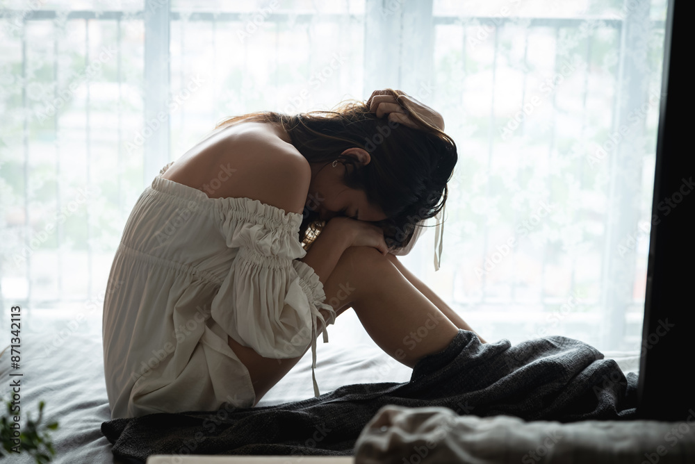 Depressed Asian woman sitting alone on the bed in dark bedroom with ...