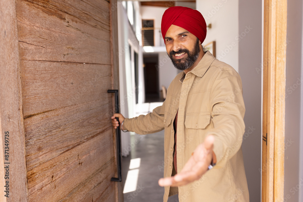 Welcoming guest, man in turban opening door and gesturing inside home, copy space Welcoming guest, man in turban opening door and gesturing inside home, copy space