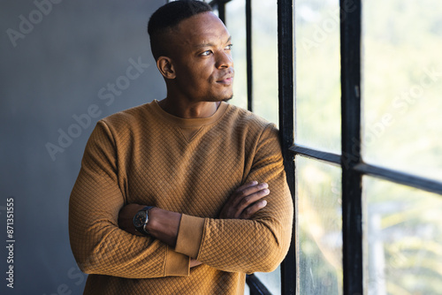 Looking out window, man in casual sweater contemplating, arms crossed