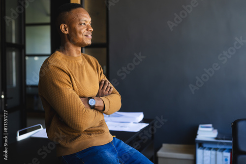 Confident businessman standing with arms crossed in modern office setting, copy space