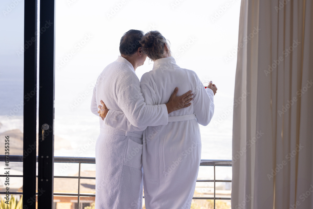 Senior couple in bathrobes embracing on balcony, enjoying ocean view Senior couple in bathrobes embracing on balcony, enjoying ocean view