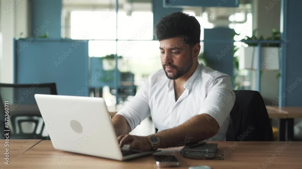 portrait of a handsome, stylish young man of Arab descent sitting in a modern business center office with a laptop, working furiously, upset by failure, closing the laptop portrait of a handsome, stylish young man of Arab descent sitting in a modern business center office with a laptop, working furiously, upset by failure, closing the laptop