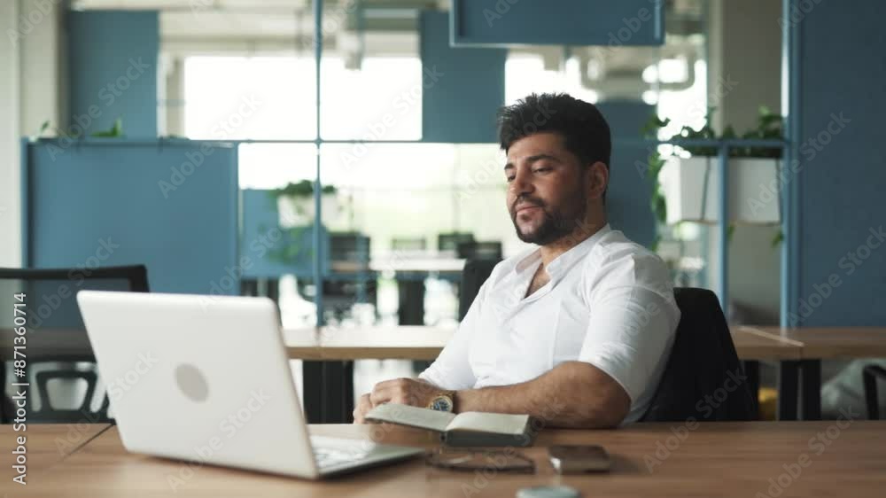 portrait of a handsome, stylish young man of Arab descent sitting in a modern business center office with a laptop, greeting and starting a video call portrait of a handsome, stylish young man of Arab descent sitting in a modern business center office with a laptop, greeting and starting a video call