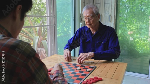 Senior asian father and son are enjoy playing checkers board game at home for leisure activities hobby and preventing from alzheimer symptom illness
