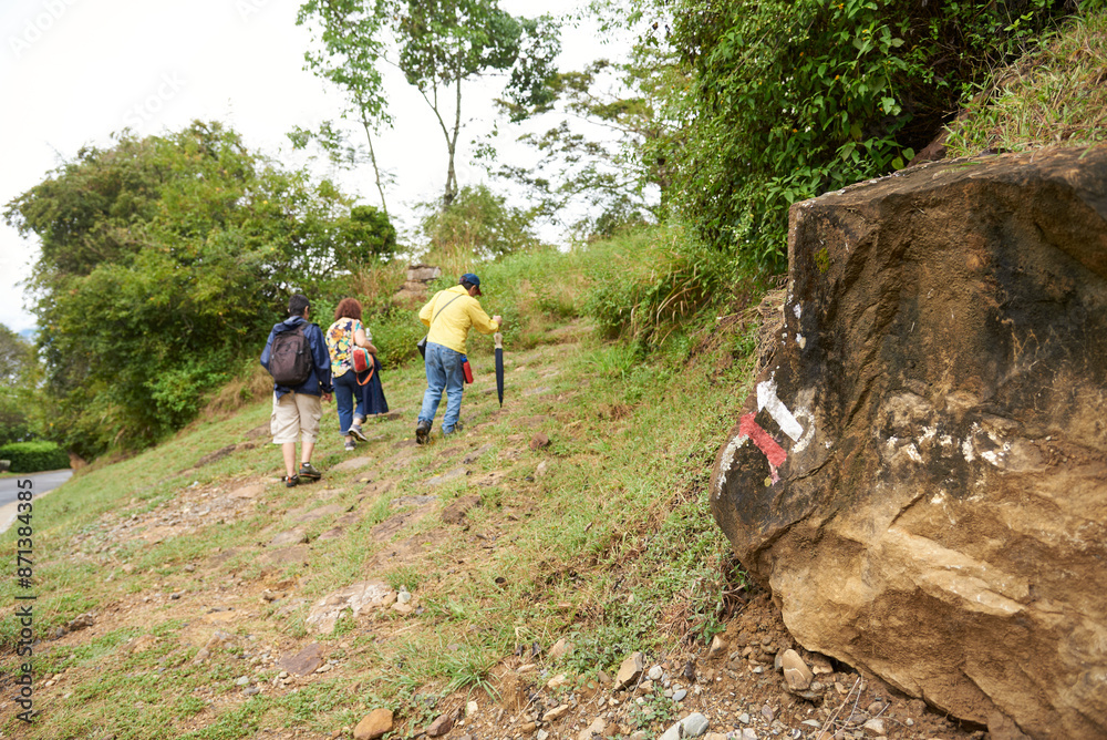 Obraz premium A group of three unrecognizable people enjoy the outdoors hiking, walking along a rural trek between Barichara and Guane, in Colombia. Color arrows painted on a rock show the correct way to the hikers