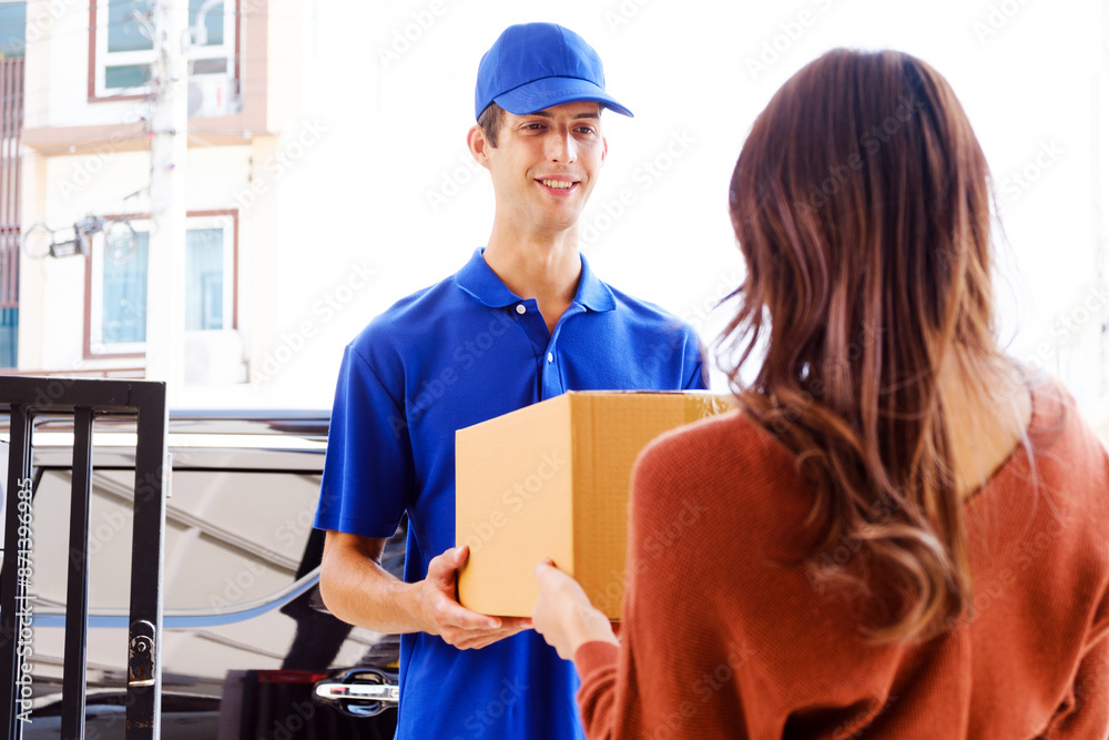Delivery man in blue uniform. A male employee in a cap t-shirt working as courier dealer hold empty cardboard box. Young courier holding parcels on doorstep. Delivery service concept Delivery man in blue uniform. A male employee in a cap t-shirt working as courier dealer hold empty cardboard box. Young courier holding parcels on doorstep. Delivery service concept