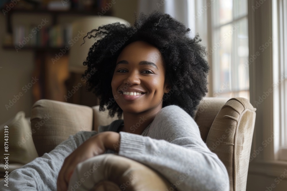 Fototapeta premium A young African American woman sits comfortably in a chair and smiles warmly.