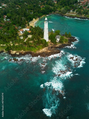 A white Dondra Head Lighthouse on the tropical cape overgrown with jungle aerial view.