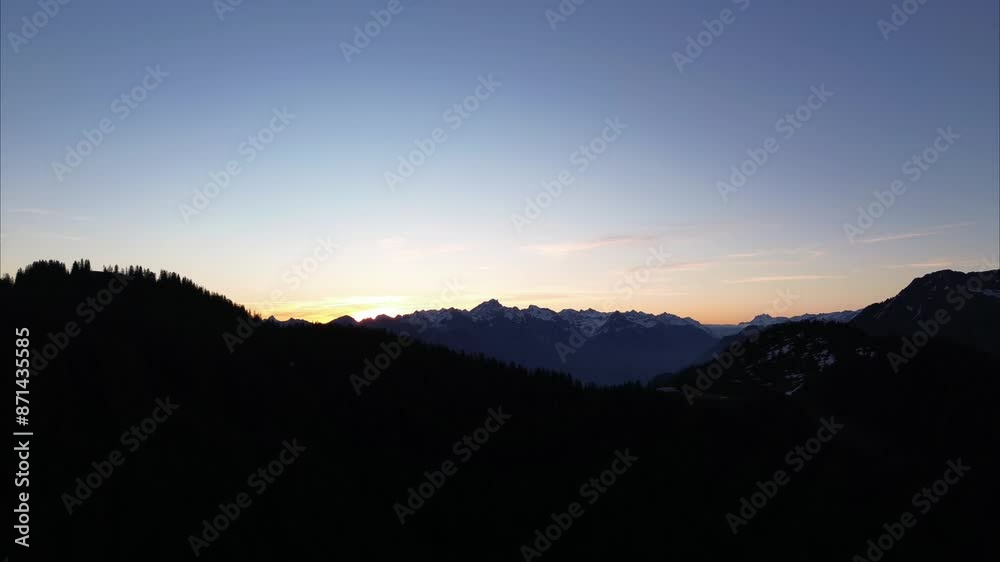 Orange Yellowish Sunrise behind Snow covered Mountain Range, with Mountains and Forest in Foreground. Bludenz, Austria, Europe Orange Yellowish Sunrise behind Snow covered Mountain Range, with Mountains and Forest in Foreground. Bludenz, Austria, Europe
