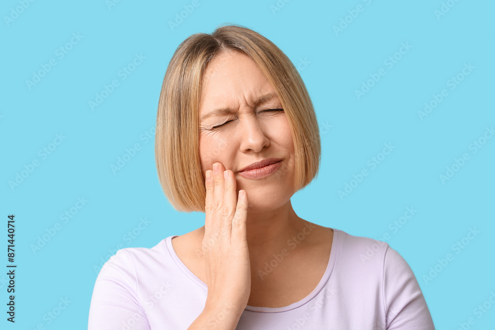 Beautiful mature woman suffering from toothache on blue background Beautiful mature woman suffering from toothache on blue background