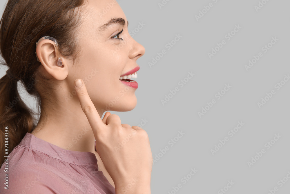 Beautiful young woman pointing at hearing aid on grey background Beautiful young woman pointing at hearing aid on grey background