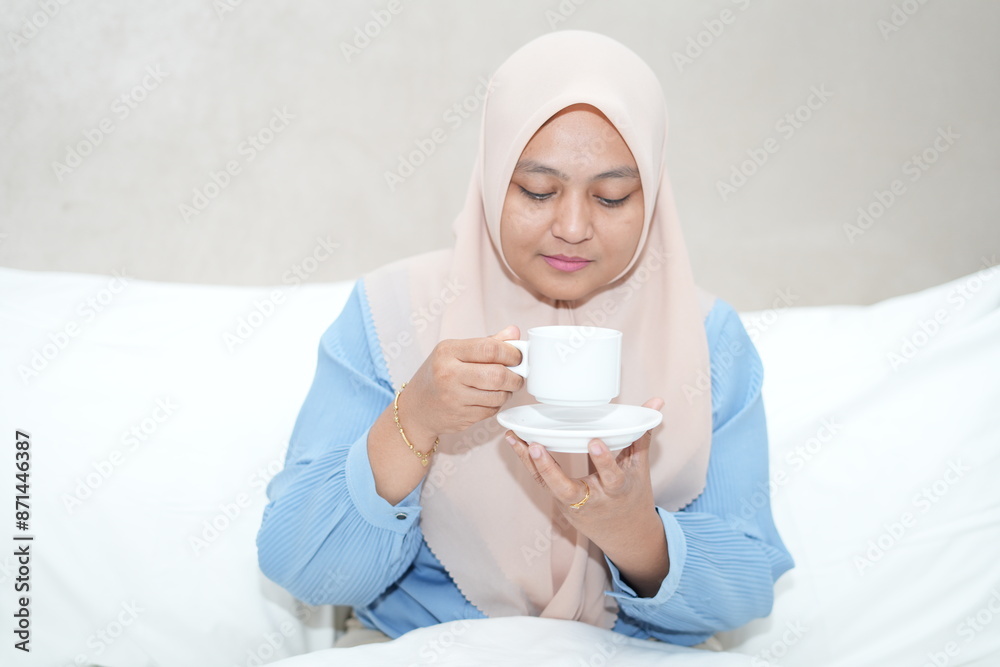 Muslim woman is relaxing while enjoying a cup of tea on the bed Muslim woman is relaxing while enjoying a cup of tea on the bed