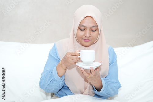 Muslim woman is relaxing while enjoying a cup of tea on the bed