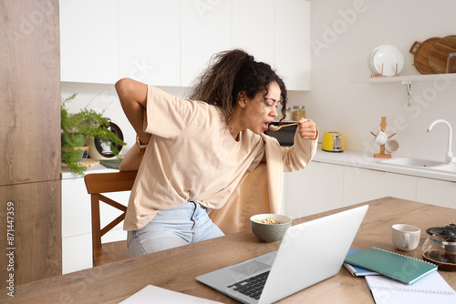 Hurrying African-American businesswoman eating breakfast and putting on blazer in kitchen