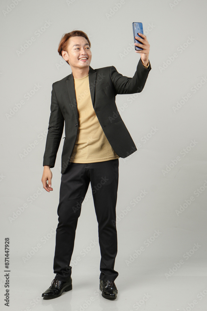 full length shoot of cheerful happy asian business man wearing suit holding mobile phone on isolated background. full length shoot of cheerful happy asian business man wearing suit holding mobile phone on isolated background.