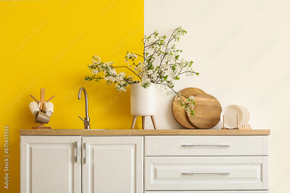Vase with blooming branches on white counter in yellow kitchen Vase with blooming branches on white counter in yellow kitchen