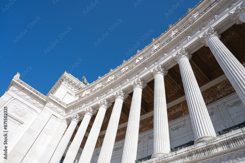 A low-angle view of the white marble columns of the Vittoriano monument in Rome, Italy, against a clear blue sky. A low-angle view of the white marble columns of the Vittoriano monument in Rome, Italy, against a clear blue sky.