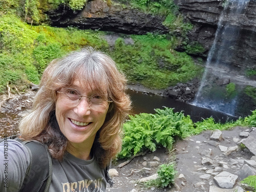 Solo traveller takes a selfie during her hike. She is wearing a t-shirt and enjoying the remote location. Henrhyd is the highest waterfall in South Wales. photo