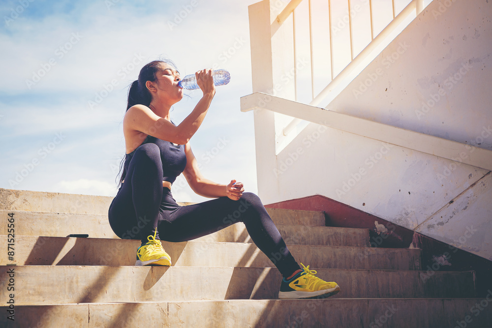 © Panumas - Tired runner woman with a bottle of electrolyte drink freshness after training outdoor workout at the stadium stairway.