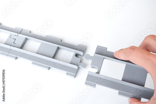 Hand holding gray toy railroad tracks put on a white background. Hand holding the tpy railroad tracks to connect them together for the concept of connection and disconnect.