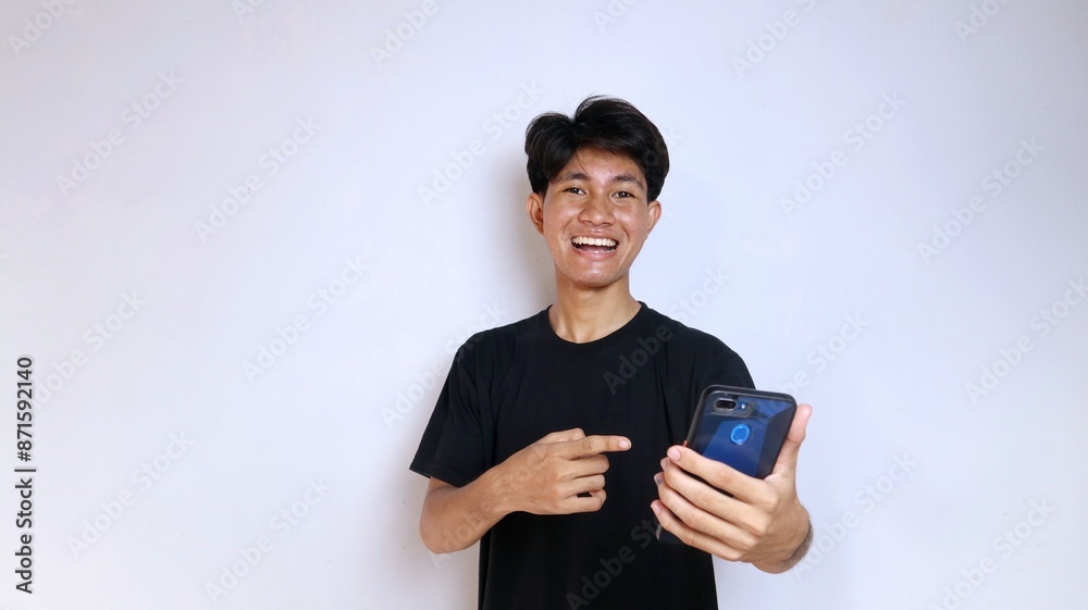 Happy young Asian man wearing black shirt gesturing pointing at smartphone Happy young Asian man wearing black shirt gesturing pointing at smartphone