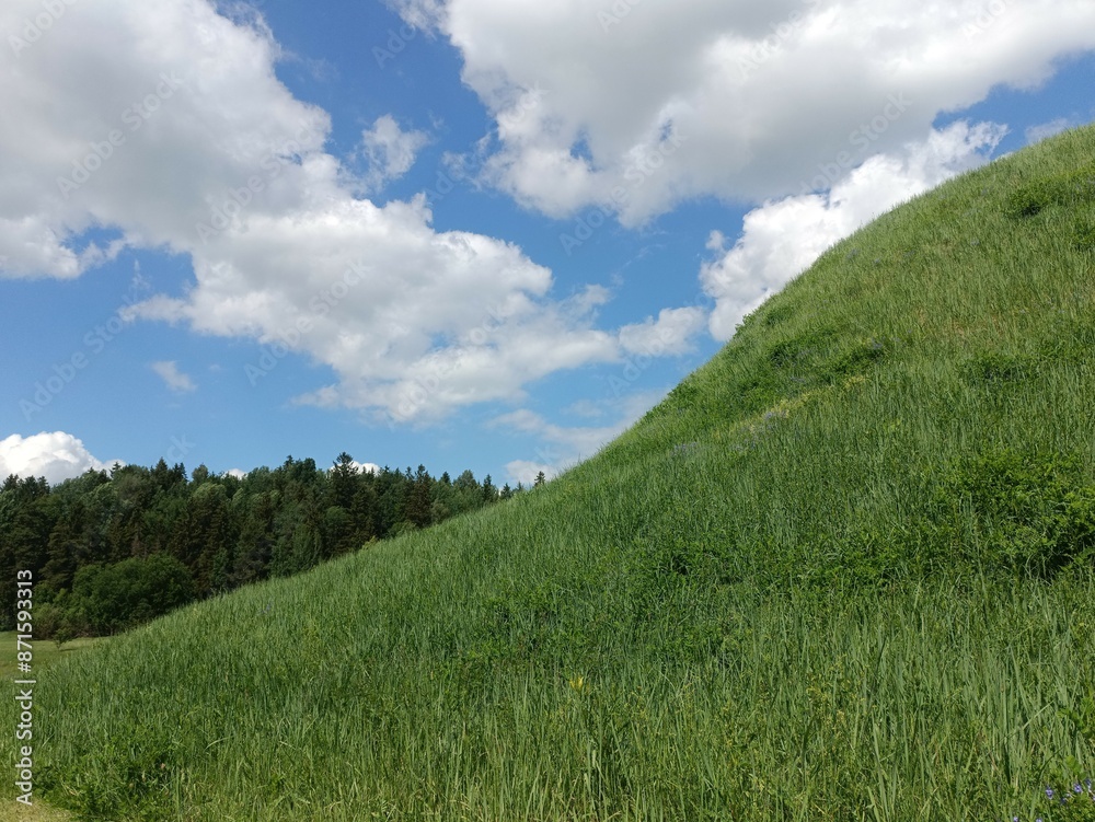 Bubiai hill during sunny day. Small hill. Grass is growing on hill. Staircase leading to the top. Sunny day with white and gray clouds in sky. Nature. Bubiu piliakalnis. Bubiai hill during sunny day. Small hill. Grass is growing on hill. Staircase leading to the top. Sunny day with white and gray clouds in sky. Nature. Bubiu piliakalnis.