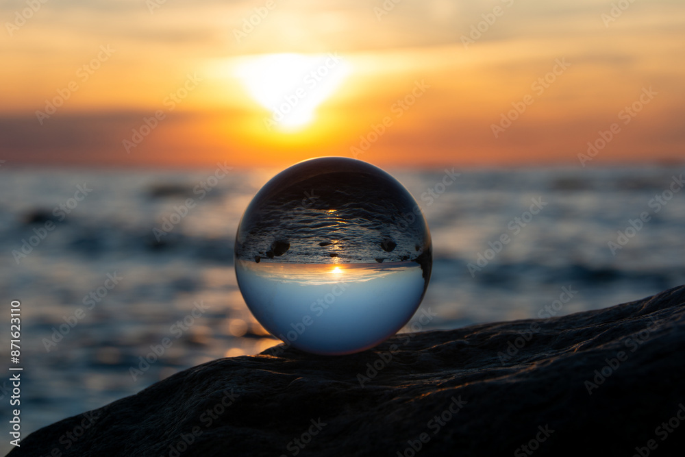 Ball made of glass lies on a stone in which the beach and the sea are reflected Ball made of glass lies on a stone in which the beach and the sea are reflected
