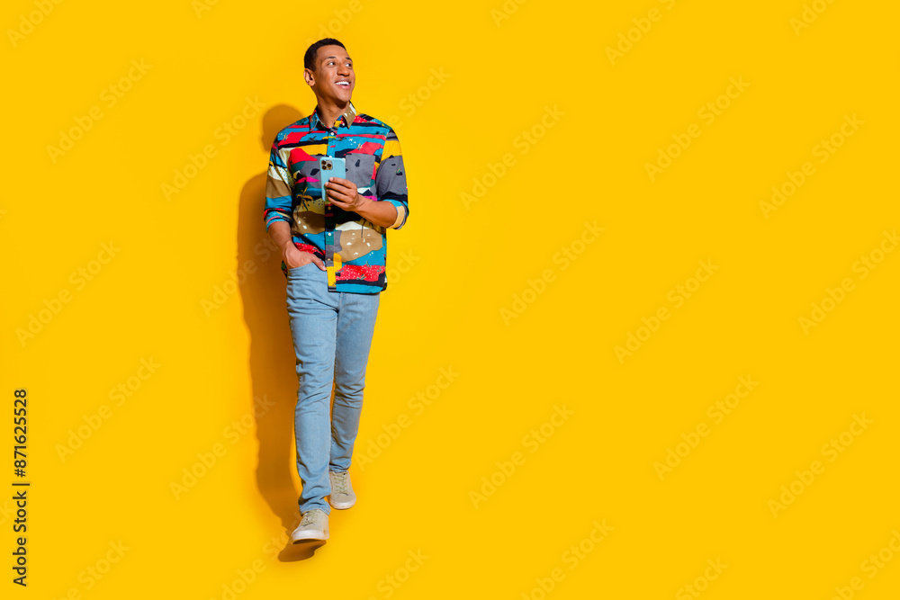Full size photo of handsome young guy look empty space hold device wear trendy colorful outfit isolated on yellow color background Full size photo of handsome young guy look empty space hold device wear trendy colorful outfit isolated on yellow color background