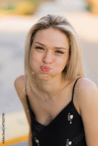 Young Caucasian blonde woman on a summer day in the city, puffing up her cheeks and making faces