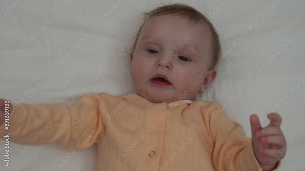 Close up sweet beautiful newborn baby in bodysuit and dry diaper lying down on white bedsheets, laughing, looks carefree plays, touches with toes. Babyhood, healthcare, paediatrics, childcare concept Close up sweet beautiful newborn baby in bodysuit and dry diaper lying down on white bedsheets, laughing, looks carefree plays, touches with toes. Babyhood, healthcare, paediatrics, childcare concept
