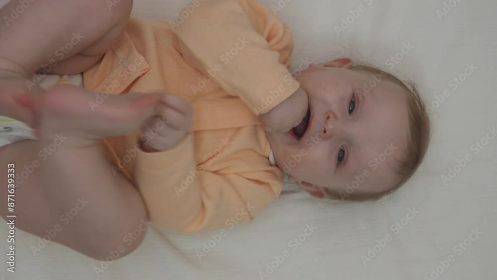 Close up sweet beautiful newborn baby in bodysuit and dry diaper lying down on white bedsheets, laughing, looks carefree plays, touches with toes. Babyhood, healthcare, paediatrics, childcare concept Close up sweet beautiful newborn baby in bodysuit and dry diaper lying down on white bedsheets, laughing, looks carefree plays, touches with toes. Babyhood, healthcare, paediatrics, childcare concept