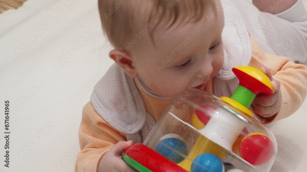 Adorable happy blonde infant baby playing with kids toys at home while sitting on carpet floor in living room. Portrait of smiling cute child toddler using colorful toys, copy space
