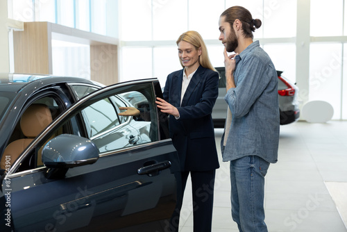 Female sale assistant in a dealership showing a new car to the customer © zinkevych