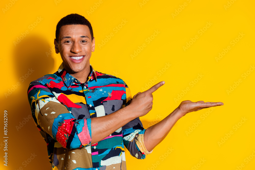 Photo portrait of attractive young man point hold empty space dressed stylish colorful clothes isolated on yellow color background Photo portrait of attractive young man point hold empty space dressed stylish colorful clothes isolated on yellow color background