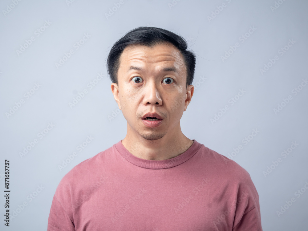 A man in a pink shirt looks upwards with a confused and puzzled expression, his eyebrows raised and mouth slightly open. The plain light blue background emphasizes his bewildered demeanor. A man in a pink shirt looks upwards with a confused and puzzled expression, his eyebrows raised and mouth slightly open. The plain light blue background emphasizes his bewildered demeanor.