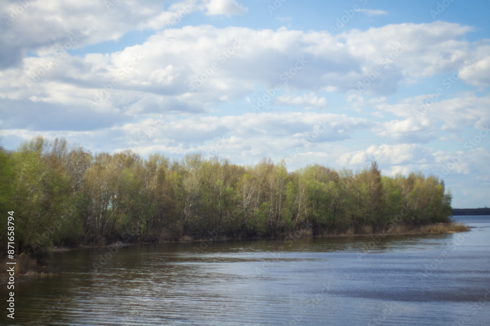 Deciduous forest on the river bank and blue sky with clouds above it. Deciduous forest on the river bank and blue sky with clouds above it.