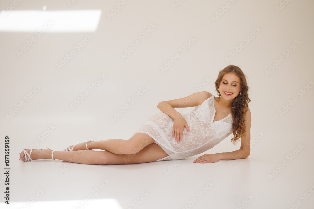 Beautiful pregnant woman in white retro underwear lace dress and white sandals with high heels. Big pregnant belly. Pretty woman waiting child. Light play on woman's body and face