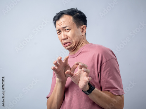 Fotografi A man in a pink shirt makes a disgusted and fearful expression with his hands raised in a defensive gesture