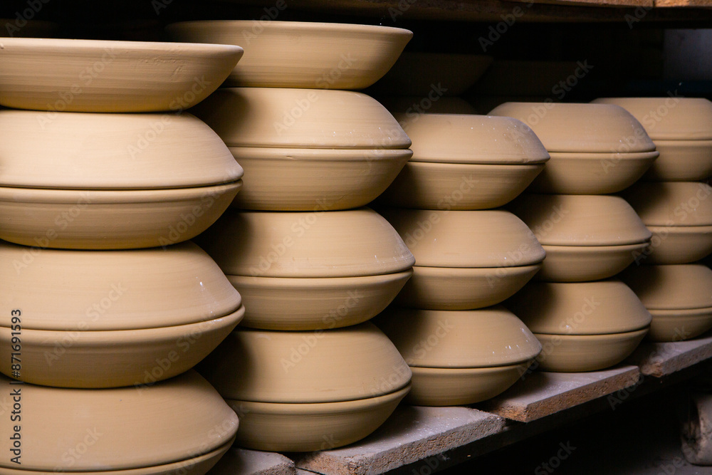 Freshly made clay mugs, pots and bowls drying up on wooden shelves in pottery workshop. Handmade ceramics manufacture. Different clay pots in workshop. Freshly made clay mugs, pots and bowls drying up on wooden shelves in pottery workshop. Handmade ceramics manufacture. Different clay pots in workshop.