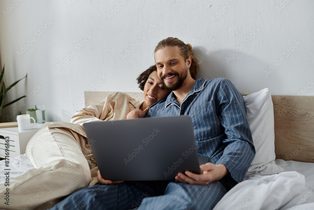 A loving couple relaxes in bed together, watching a laptop. A loving couple relaxes in bed together, watching a laptop.