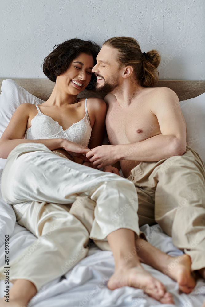 A couple shares a tender moment of laughter while lying in bed together. A couple shares a tender moment of laughter while lying in bed together.
