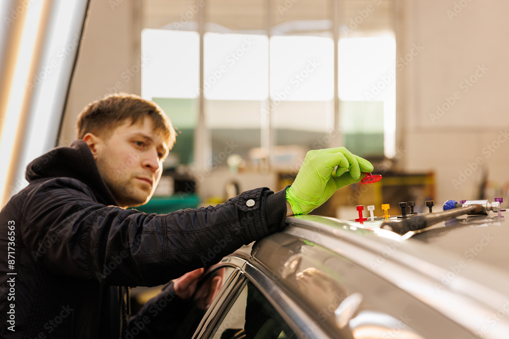 A man in green gloves gestures while working on a car in a garage A man in green gloves gestures while working on a car in a garage