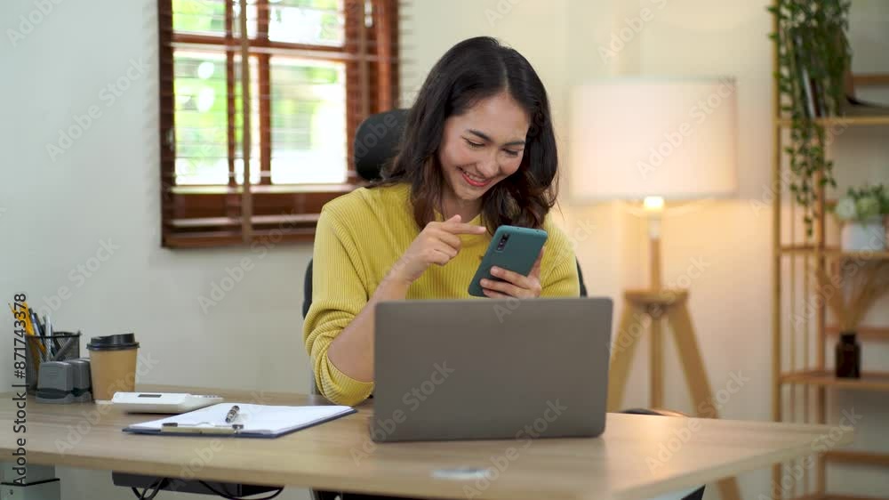 Happy Asian businesswoman sitting in the office with her laptop computer working diligently and smiling brightly with loads of papers on her desk. Happy Asian businesswoman sitting in the office with her laptop computer working diligently and smiling brightly with loads of papers on her desk.