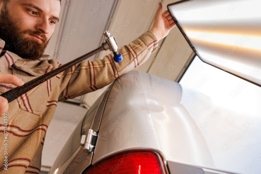 Man uses hammer to repair dent in car with Automotive lighting and gestures