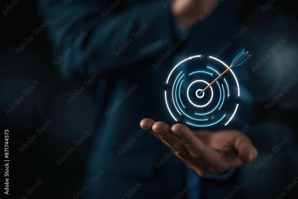Businessman holding a futuristic hologram of a target with an arrow in the middle, representing achieving a goal Businessman holding a futuristic hologram of a target with an arrow in the middle, representing achieving a goal