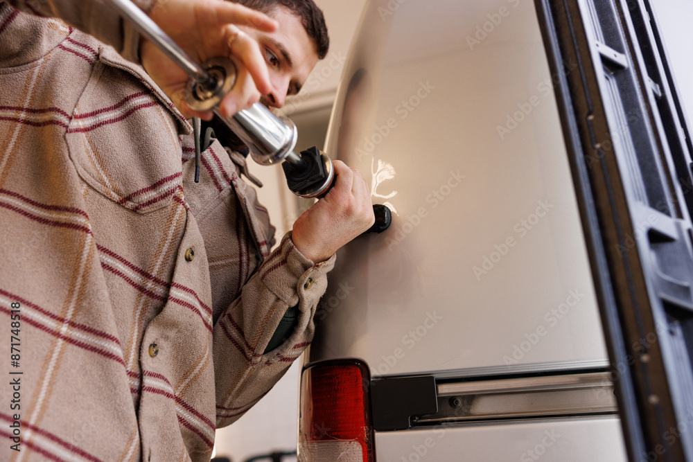 The Caucasian boy uses a special tool to strip the fender of a car