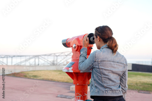 Woman looking through a red telescope at an outdoor observation deck...