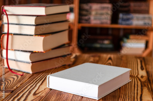 Books. A white notebook with space for text lies on a wooden table against the background of bookshelves