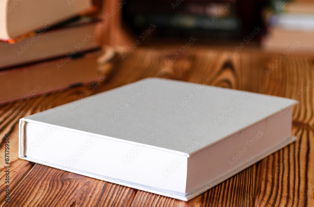 Fototapeta premium Books. A white notebook with space for text lies on a wooden table against the background of bookshelves